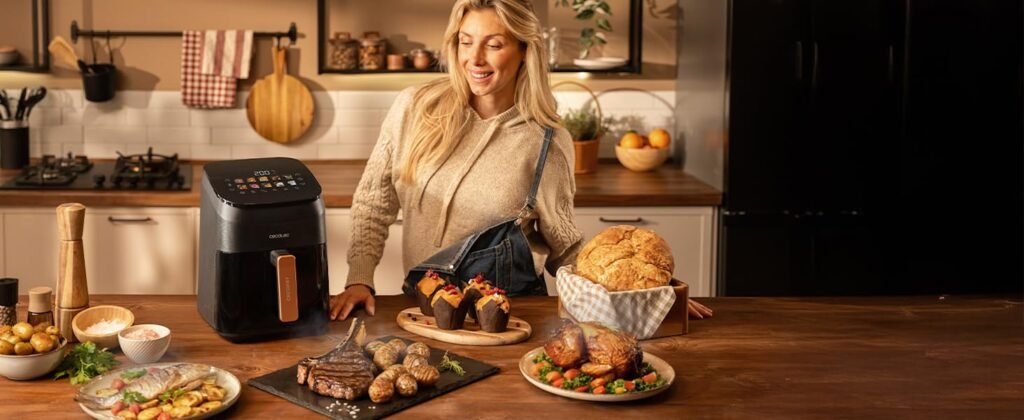 Mujer en cocina moderna con freidora Cecotec Smokin'Heat 4000 sobre la encimera y platos variados como muffins, pollo asado y filete con patatas